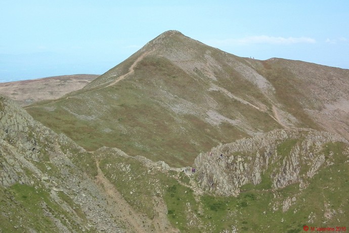 Walkers on the rock step of Striding Edge, with Catstye Cam beyond.