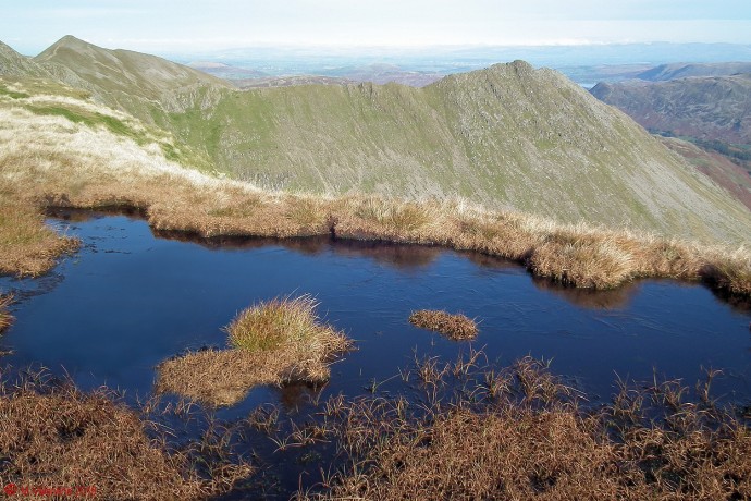 An ice covered bog-pool on Nethermost Pike summit ridge, with Striding Edge beyond.